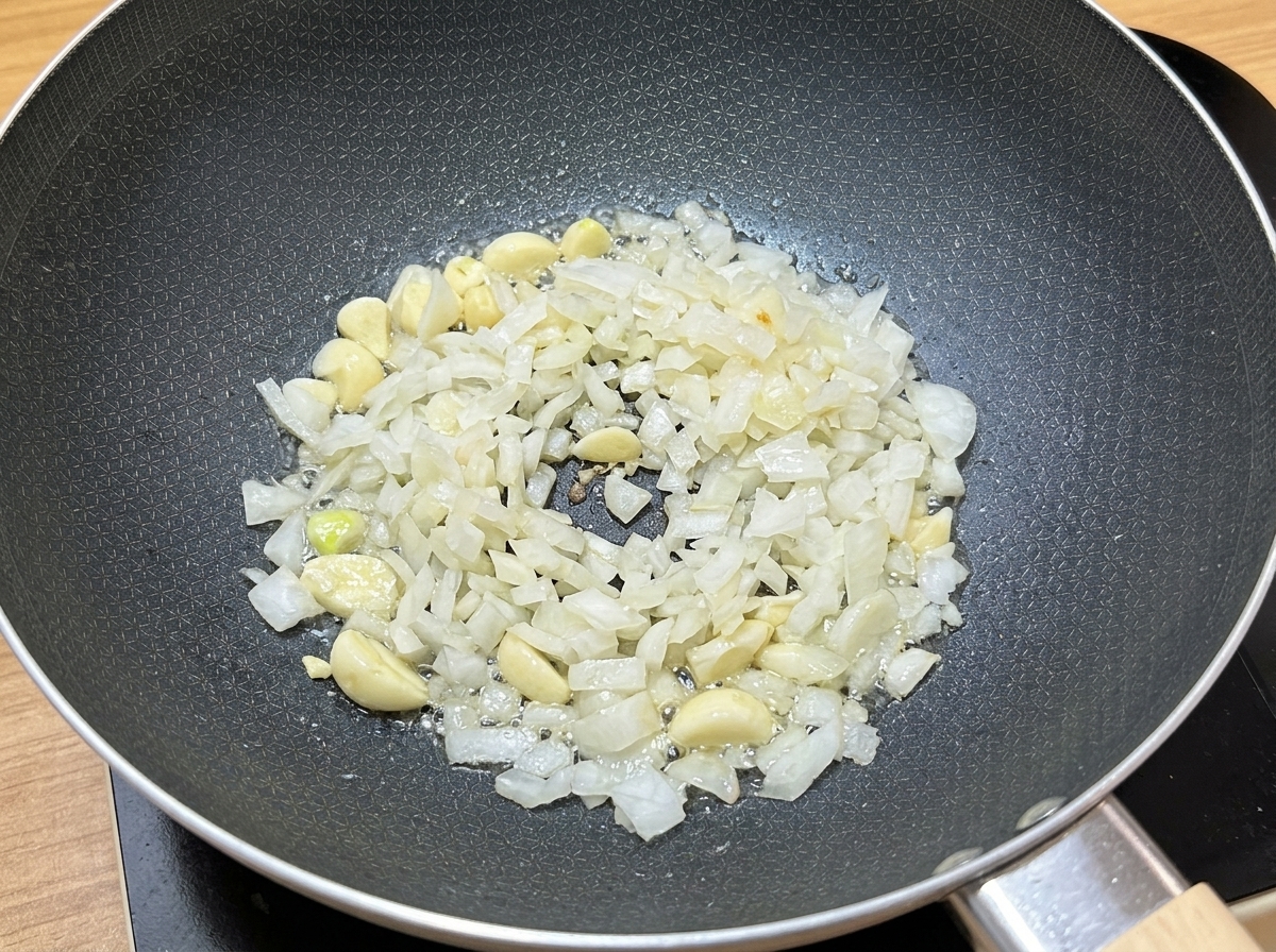 Gehackter Knoblauch und Zwiebelwürfel brutzeln in Speiseöl in einer dunklen Pfanne.