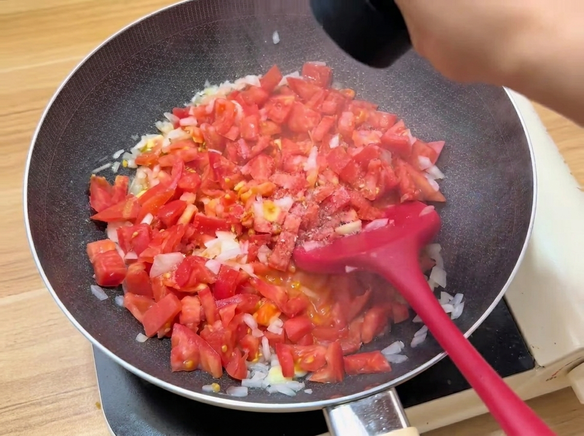 Gewürfelte Tomaten werden in einer Pfanne gekocht und gewürzt.