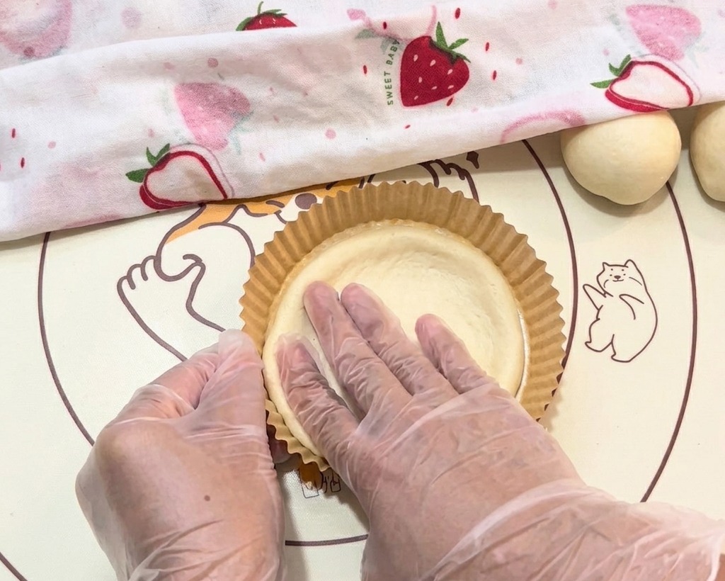 Der Teig wird mit behandschuhten Händen vorsichtig in eine Papierschale gedrückt.