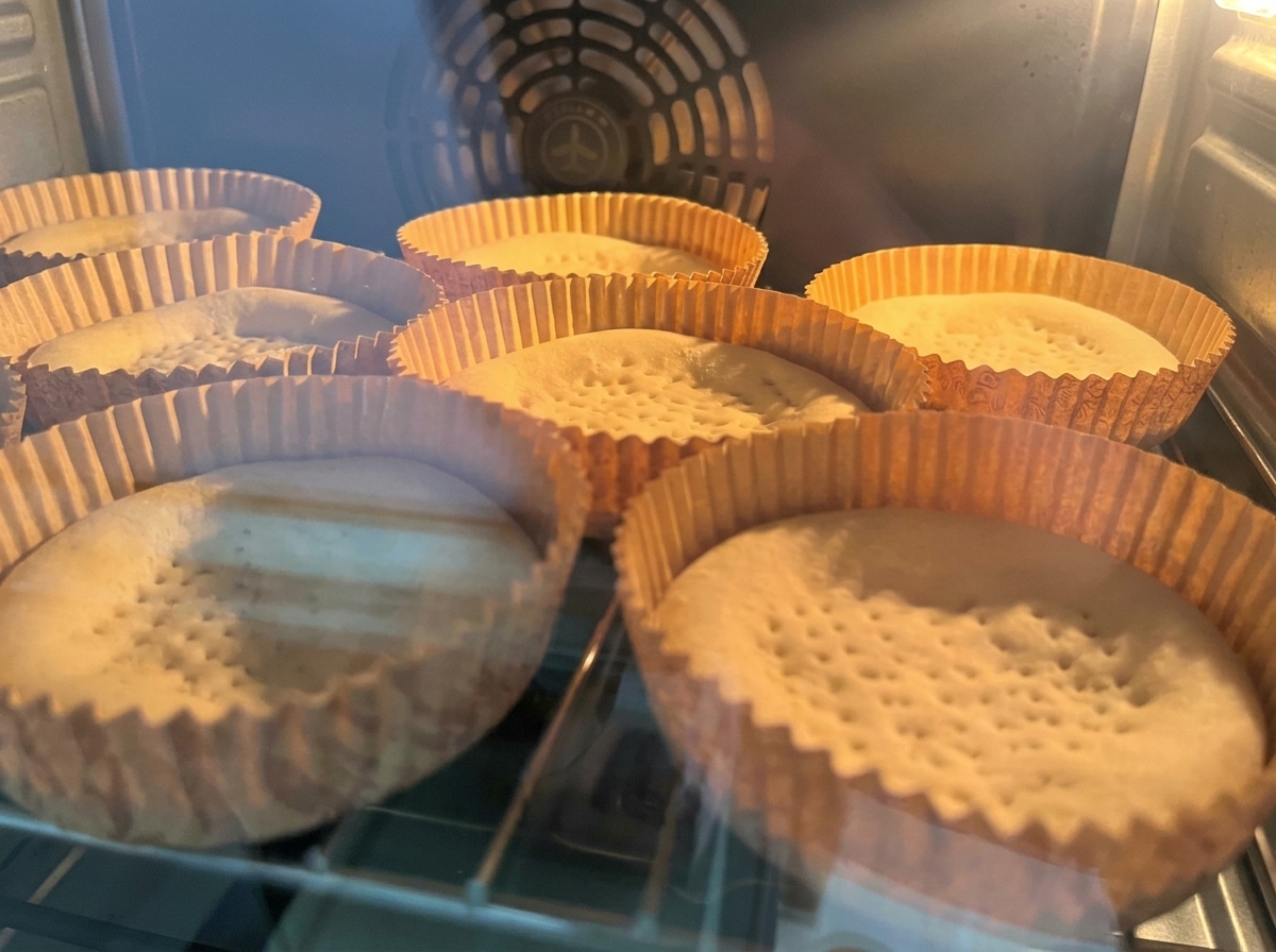 Leere Pizzaböden backen in ihren Förmchen im beleuchteten Ofen.