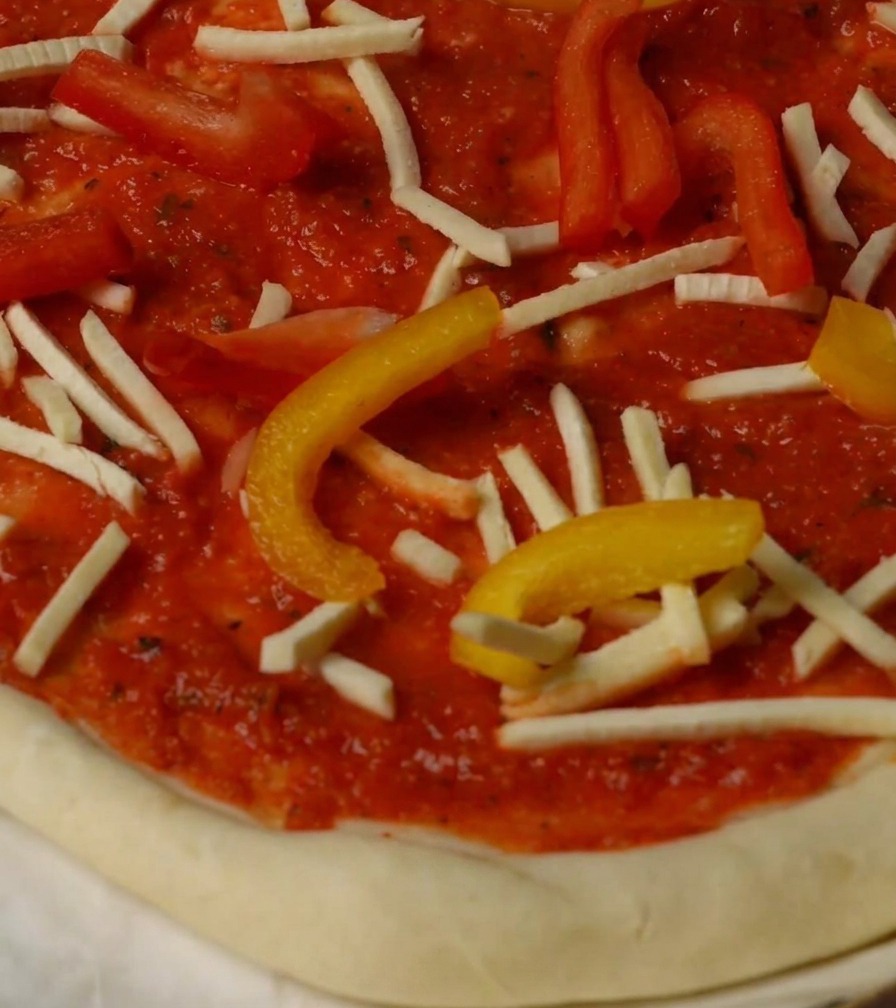 Pizza belegt mit Paprika, Käse und Hummerstücken vor dem Backen.