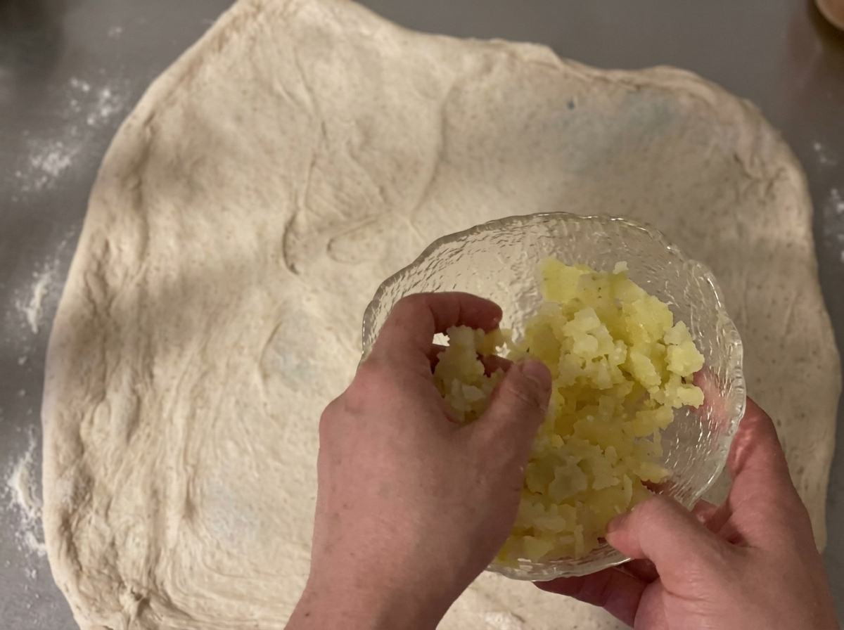 Gewürfelte Kartoffeln und geriebener Cheddar-Käse werden über ein ausgerolltes Stück rohen Teig gestreut.