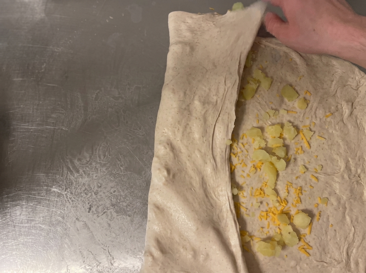Der Teig wird auf der Arbeitsfläche aufgerollt, um die Käse- und Kartoffelfüllung im Inneren zu sichern.