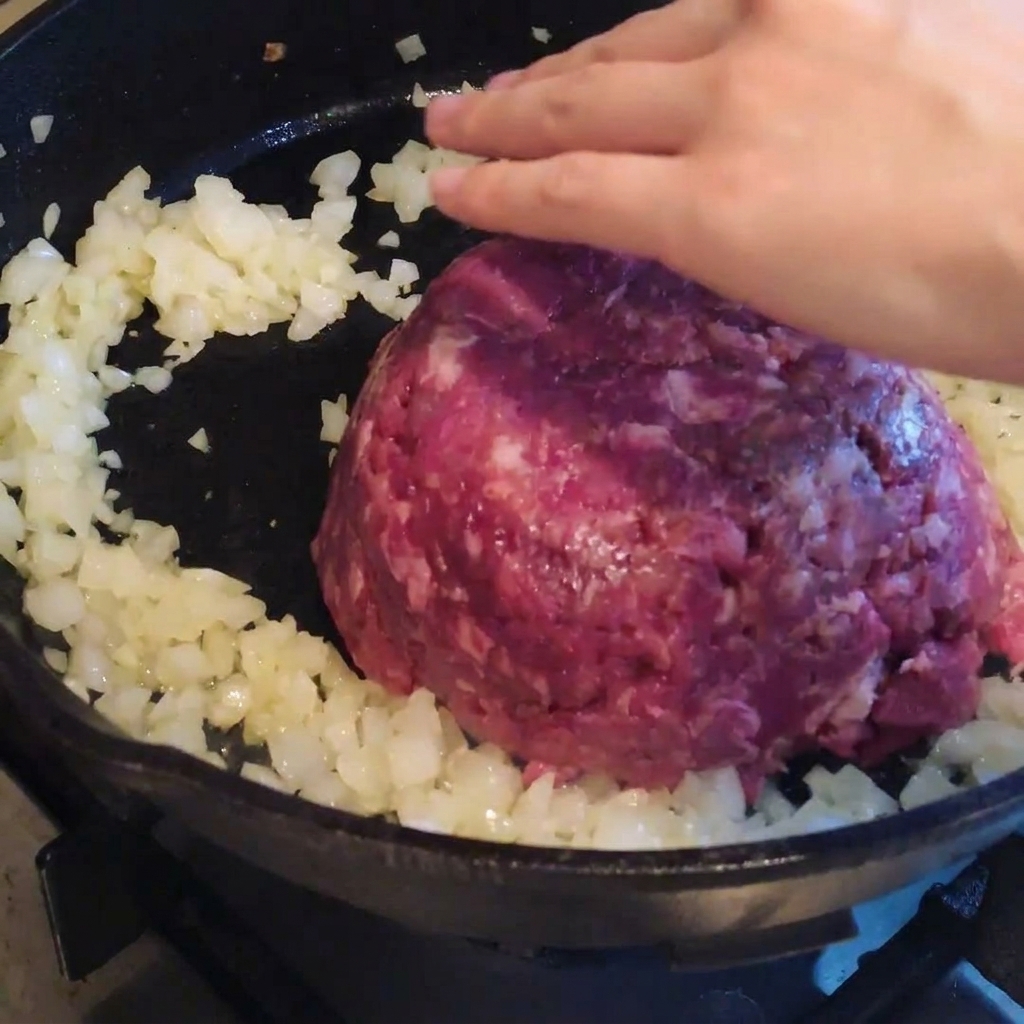 Rinderhackfleisch wird zu den Zwiebeln in die Pfanne gegeben und gewürzt.