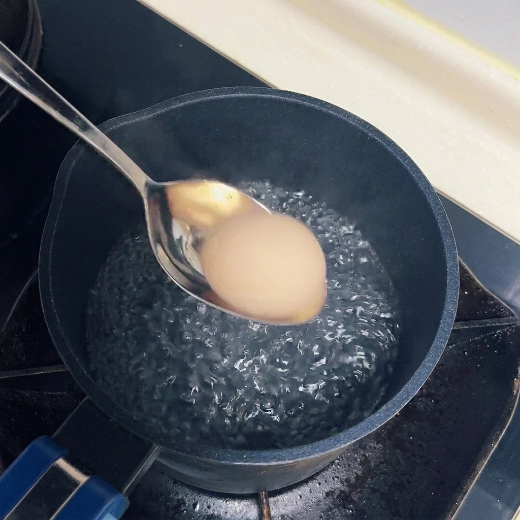 Ein Ei wird vorsichtig mit einem Metalllöffel in einen Topf mit leicht siedendem Wasser gegeben.