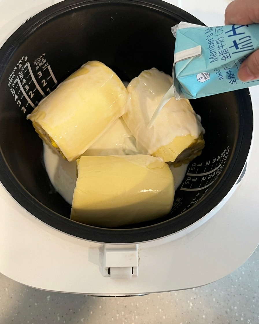 Milch wird aus einem Karton in einen Reiskocher mit Mais und Käse gegossen.