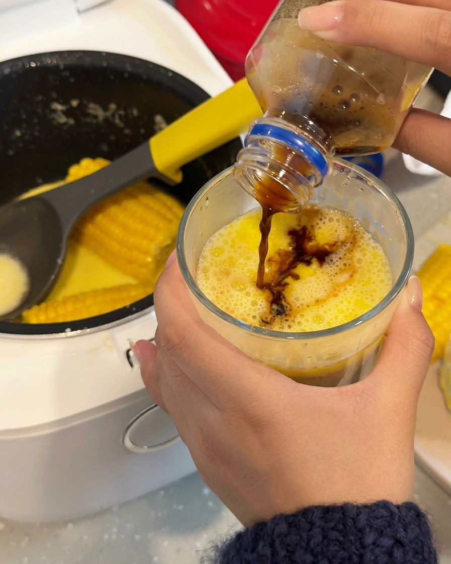 Dunkler Kaffee wird in ein Glas mit einer leuchtend gelben, milchigen Maisbrühe gegossen.