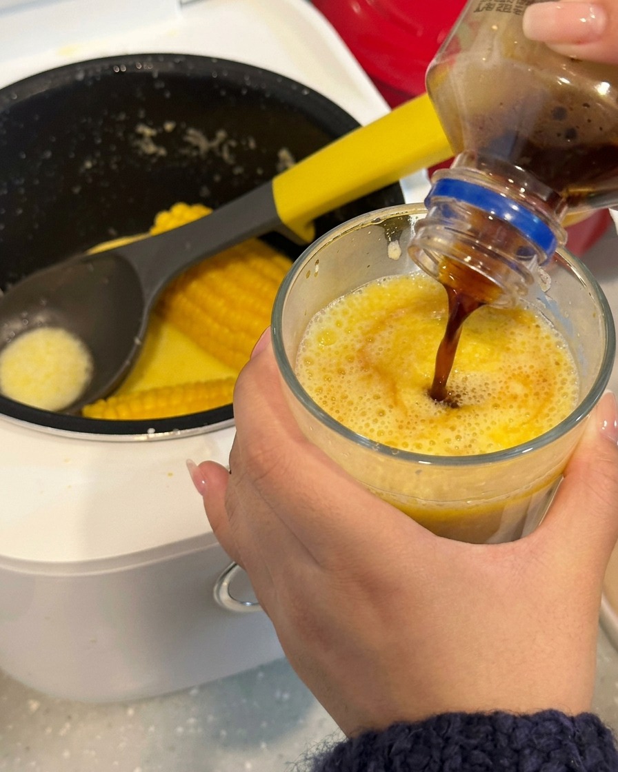 Nahaufnahme eines Holzstäbchens, das eine Kaffee-Mais-Mischung in einem klaren Glas umrührt.