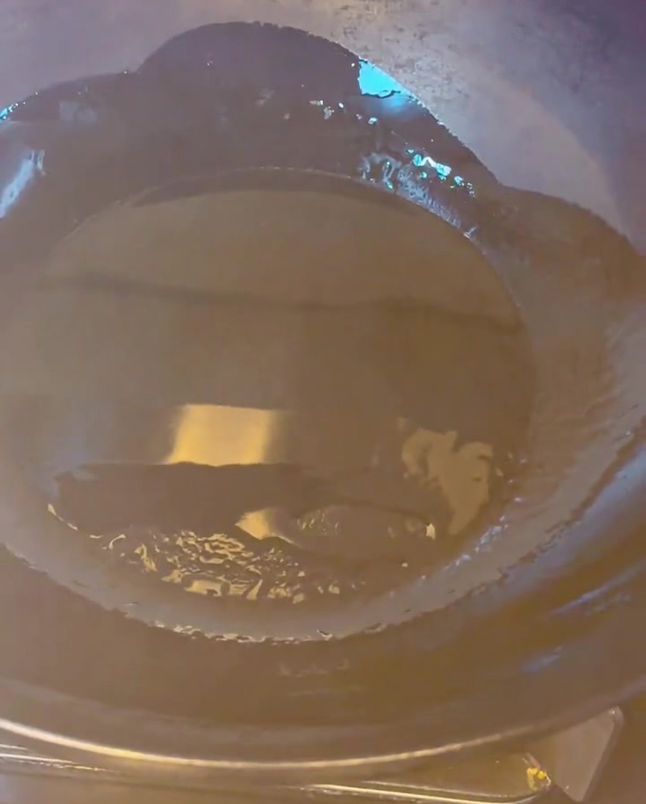 Goldbraune Schweinebauchstücke werden in einem heißen Wok mit Öl angebraten.