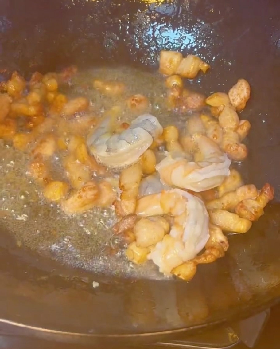 Garnelen, Schweinebauch und verschiedene Meeresfrüchte, die zusammen in einem heißen Wok gebraten werden.