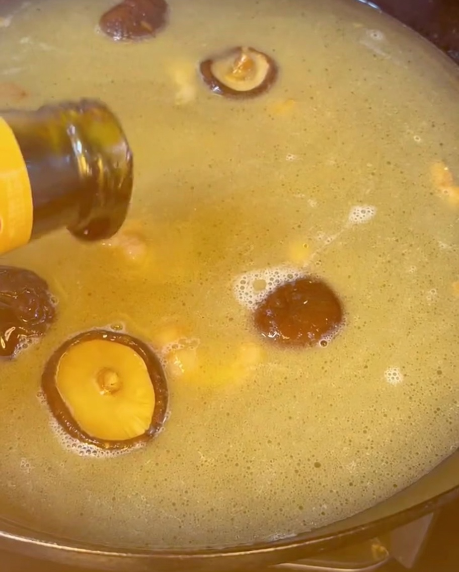 Austernsauce wird aus einer Flasche in eine kochende, goldene Brühe mit Shiitake-Pilzen gegossen.