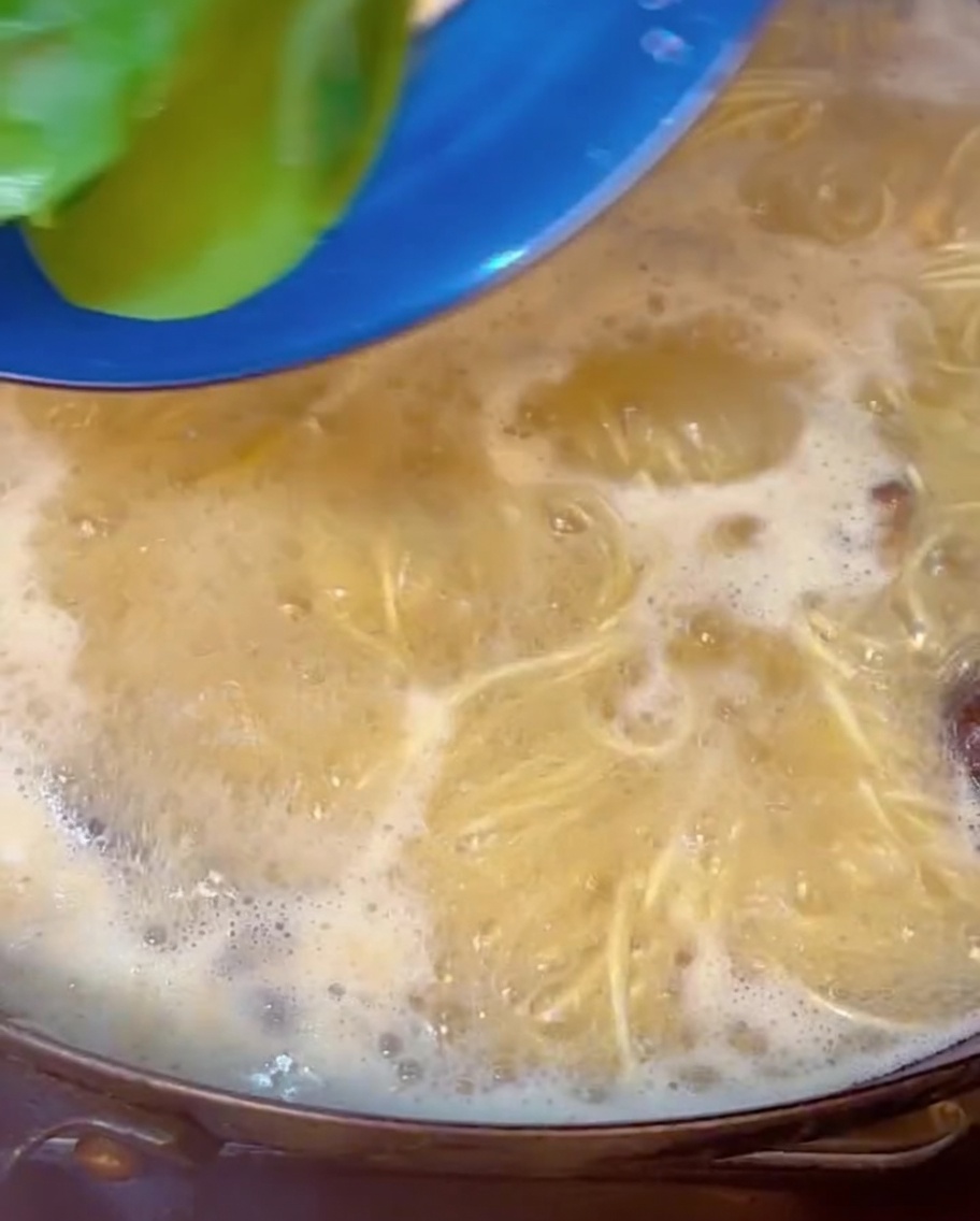 Frischer, grüner Pak Choi wird in einen Topf mit blubbernder Brühe und Ramen-Nudeln getaucht.