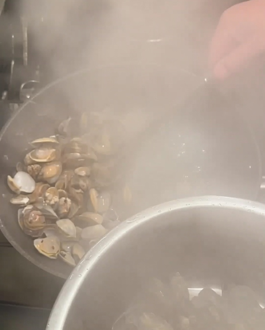 Geöffnete Muscheln werden mit einer Schaumkelle aus dem kochenden Topf geholt.