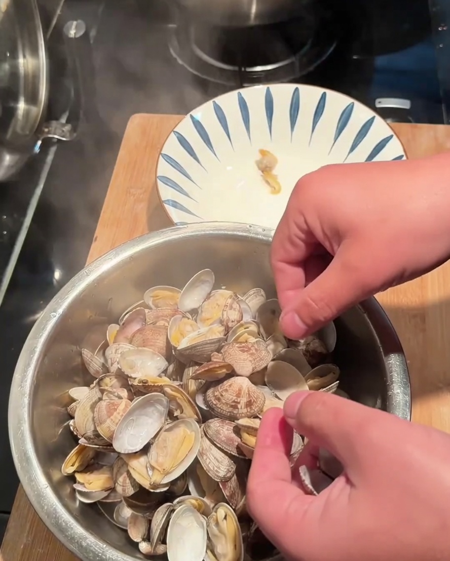 Hände lösen das Muschelfleisch aus den gekochten Schalen in eine Schüssel.