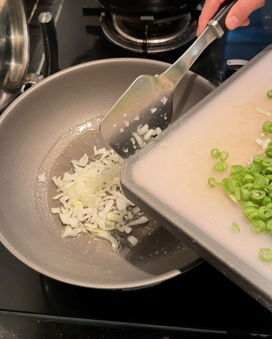Gehackte Frühlingszwiebeln und geschnittene Schlangenbohnen werden in einem heißen Wok mit Öl angebraten.