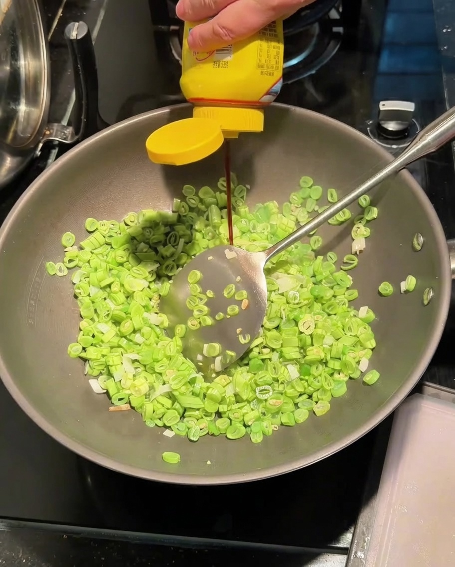 Würzsauce wird in einen Wok mit Bohnen und Frühlingszwiebeln gegeben.