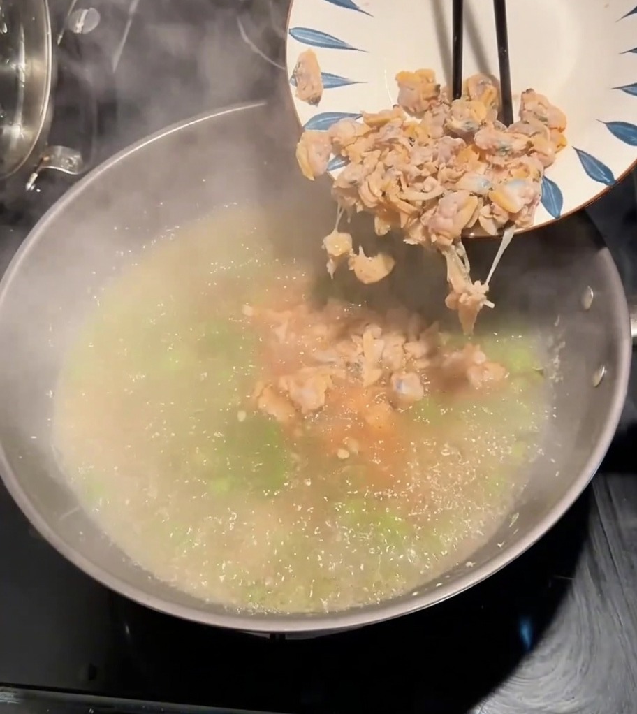Muschelfleisch wird von einem Teller in einen Topf mit kochender, gewürzter Brühe und grünem Gemüse gegeben.