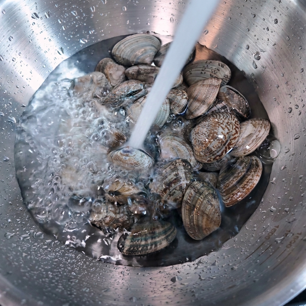 Fließendes Wasser gießt über frische Venusmuscheln in einer Edelstahlschüssel.
