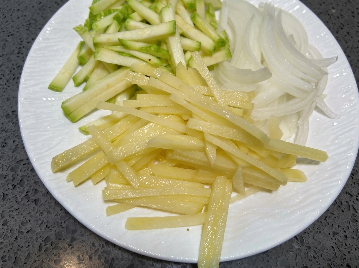Dünne Streifen von Zucchini, Zwiebeln und Kartoffeln ruhen auf einem weißen Teller.