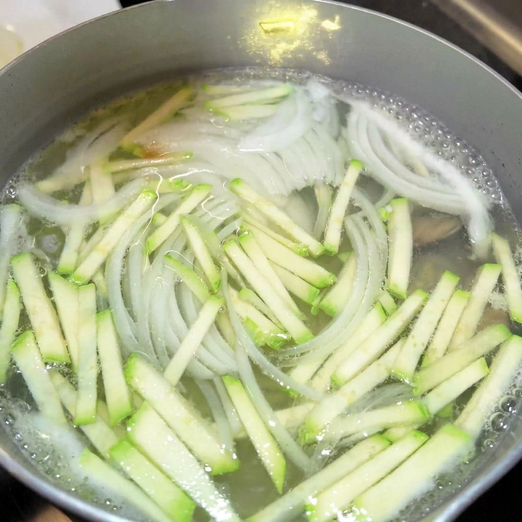 Nahaufnahme von Gewürzen wie Sojasauce und Fischsauce, die zu einem Topf mit kochender Gemüsebrühe hinzugefügt werden.