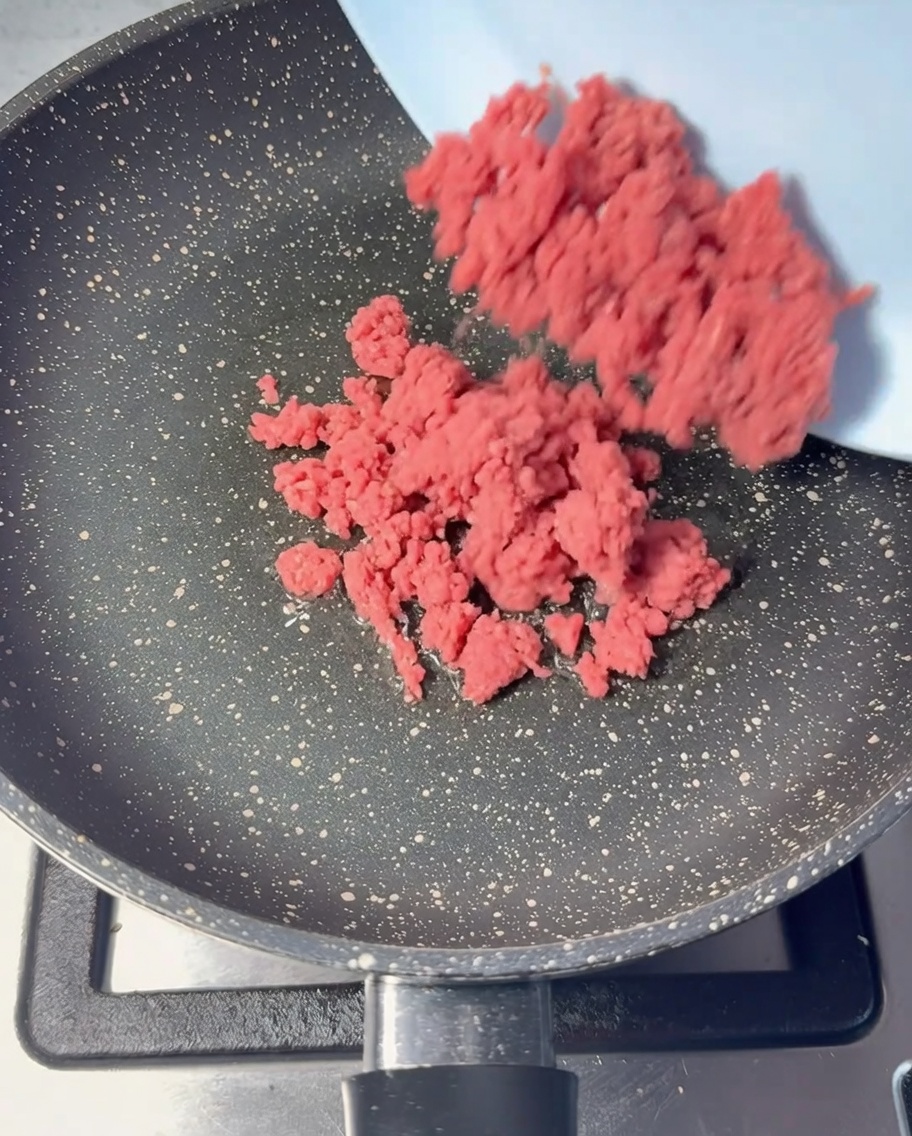 Rohes Rinderhackfleisch wird in eine geölte Pfanne gegeben.