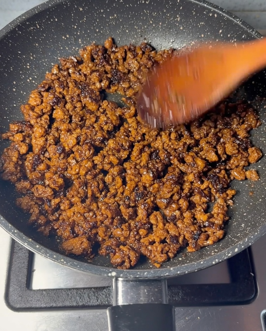Rinderhackfleisch wird in einer Pfanne mit einem Holzlöffel gebraten, bis es braun ist.