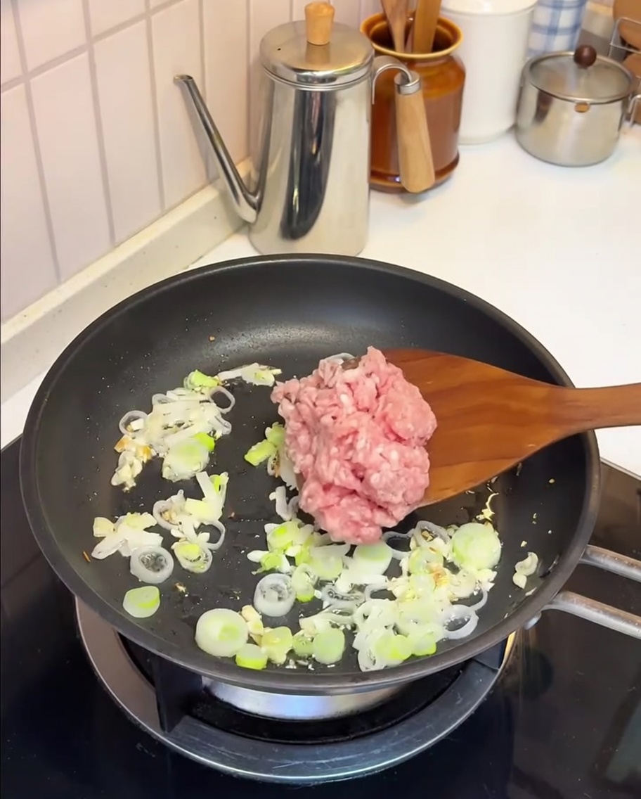 Schweinehackfleisch wird mit Knoblauch und Frühlingszwiebeln in der Pfanne angebraten.