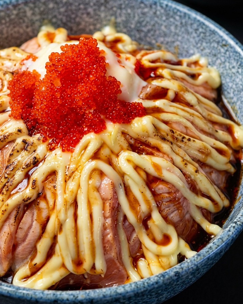 Ein Flambierbrenner röstet leicht die Oberseite einer mit Mayonnaise und Fischrogen garnierten Lachs-Bowl.