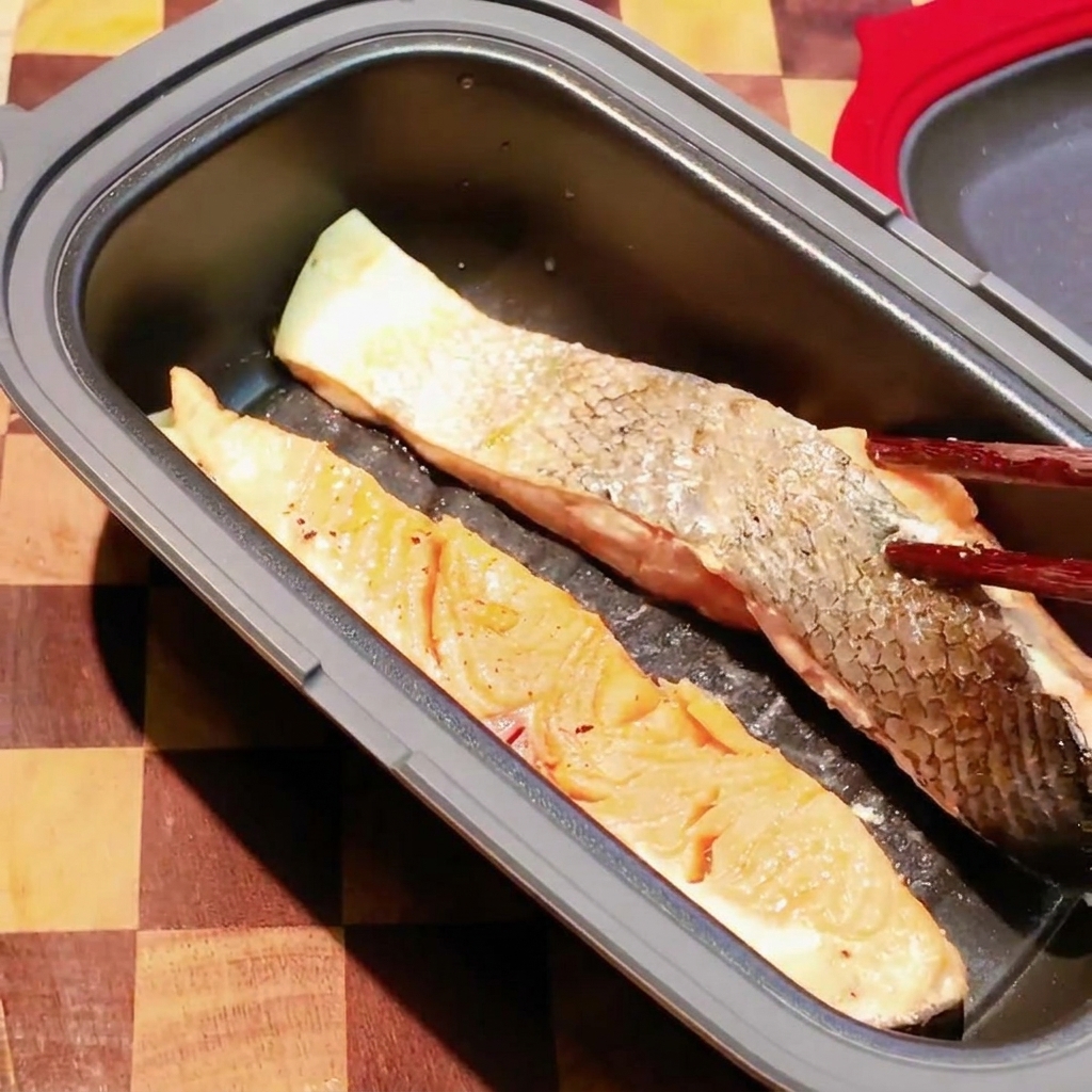 Stäbchen wenden ein teilweise gegartes Lachsfilet in einer dunklen Mikrowellen-Bratpfanne.