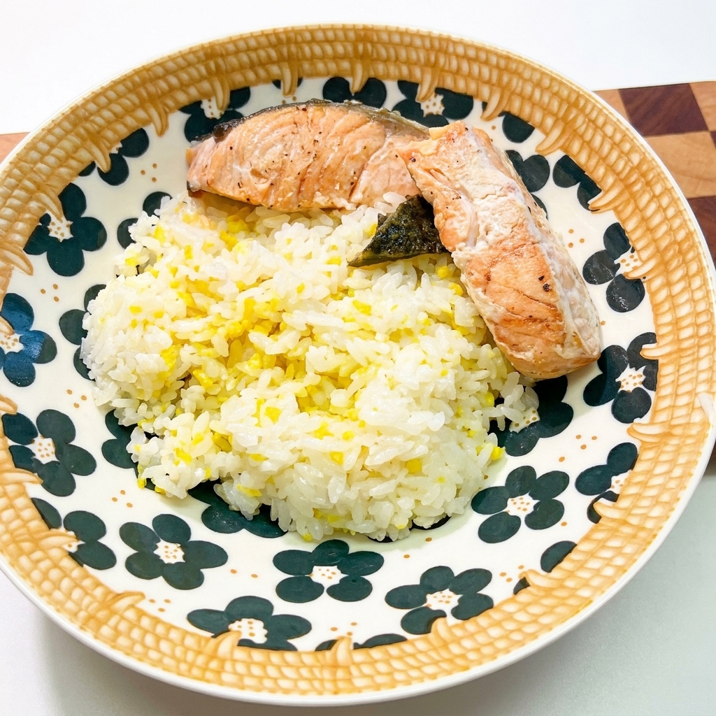 Eine hübsch gemusterte Keramikschüssel mit weißem Reis, darauf zwei Stücke gebratener Lachs und dunkle Algenflocken.