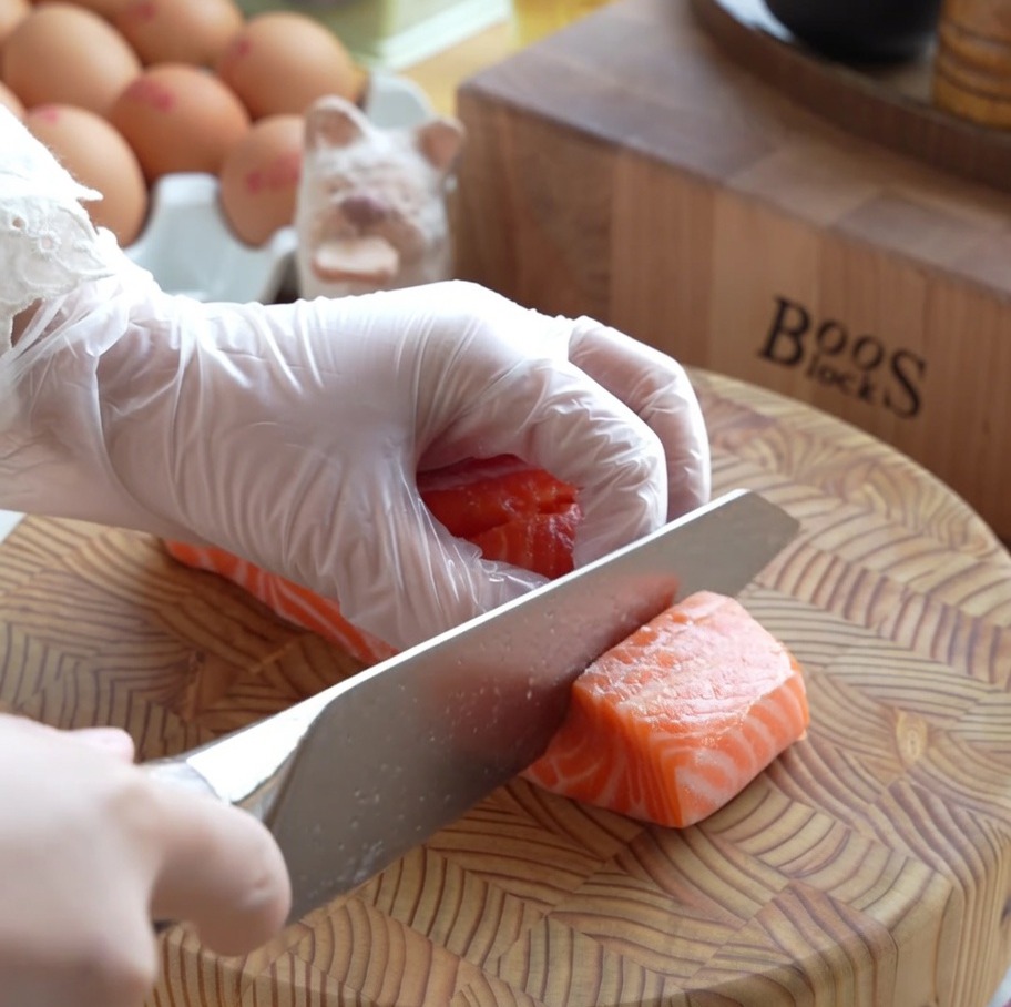 Dicke Würfel aus frischem, rohem Lachs, sauber vorbereitet auf einem Holzschneidebrett.
