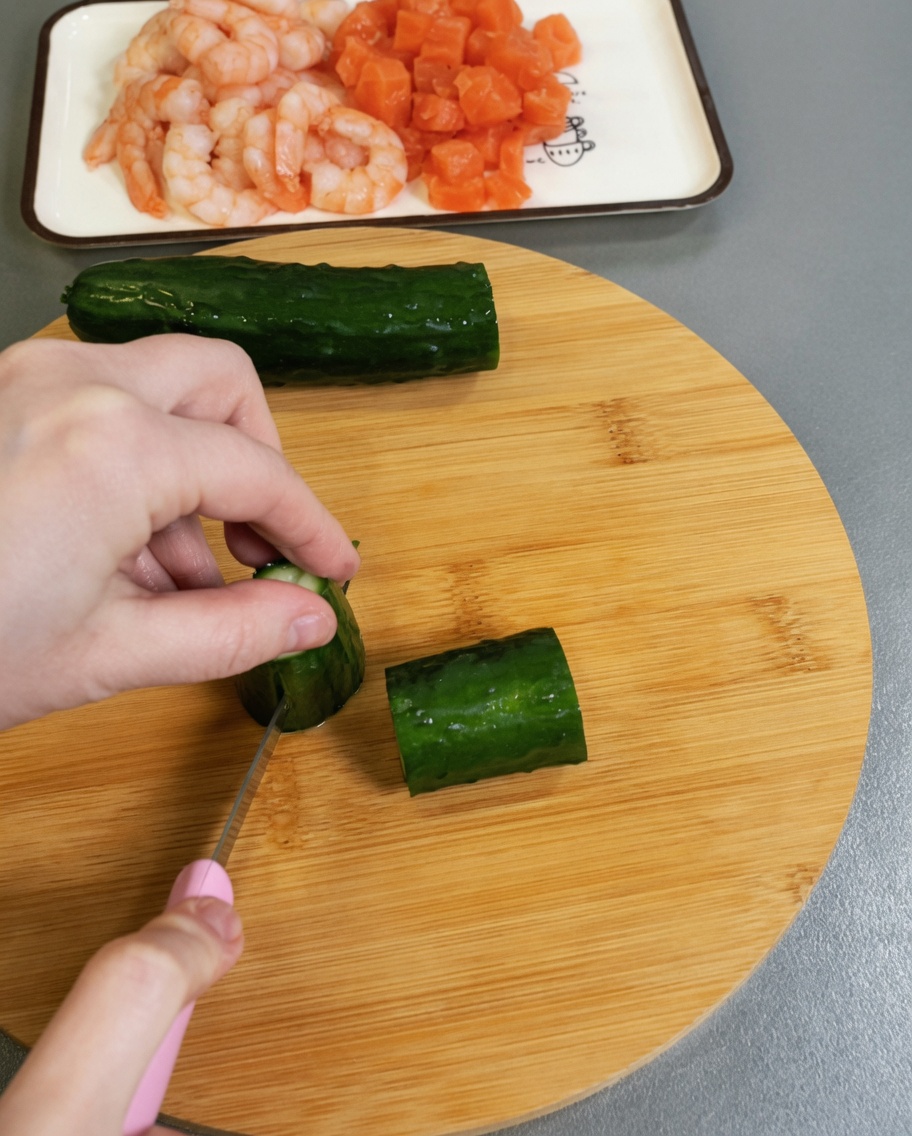 Eine frische grüne Gurke wird auf einer Holzunterlage in kleine Würfel gehackt.