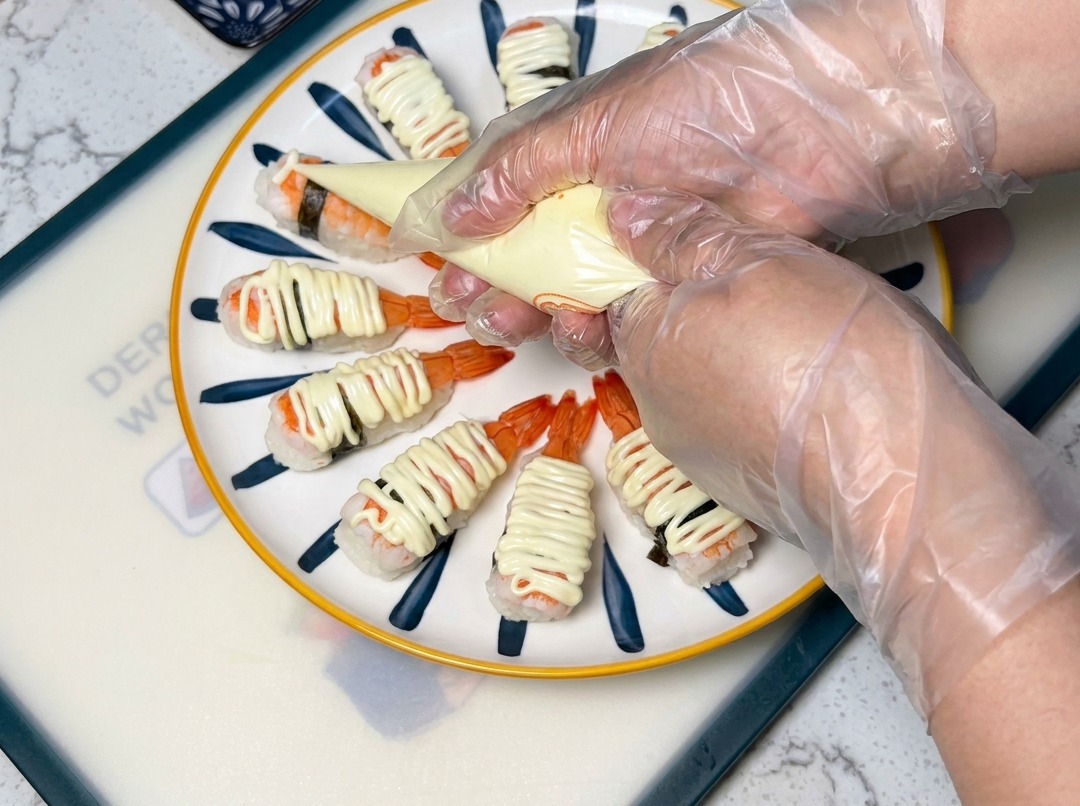 Ein Spritzbeutel gibt Mayonnaise in einem Zickzack-Muster über die Garnelen-Sushi.