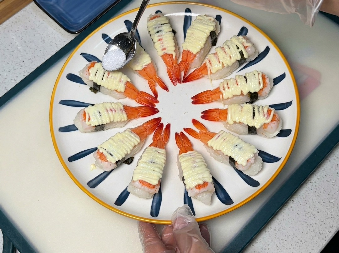 Ein Löffel streut Zucker über das mit Mayonnaise bedeckte Sushi auf einem Teller.