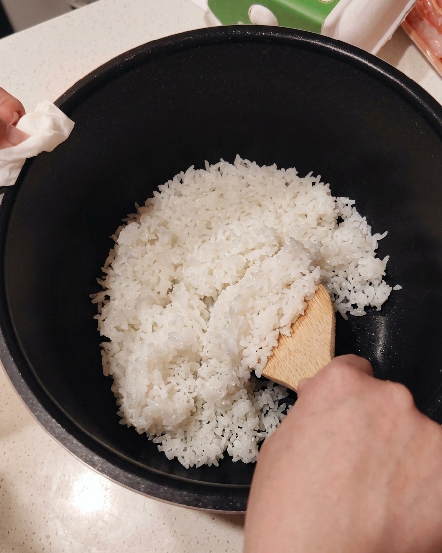 Sushi-Essig wird mit einem Holzspatel unter den frisch gekochten Reis gemischt.
