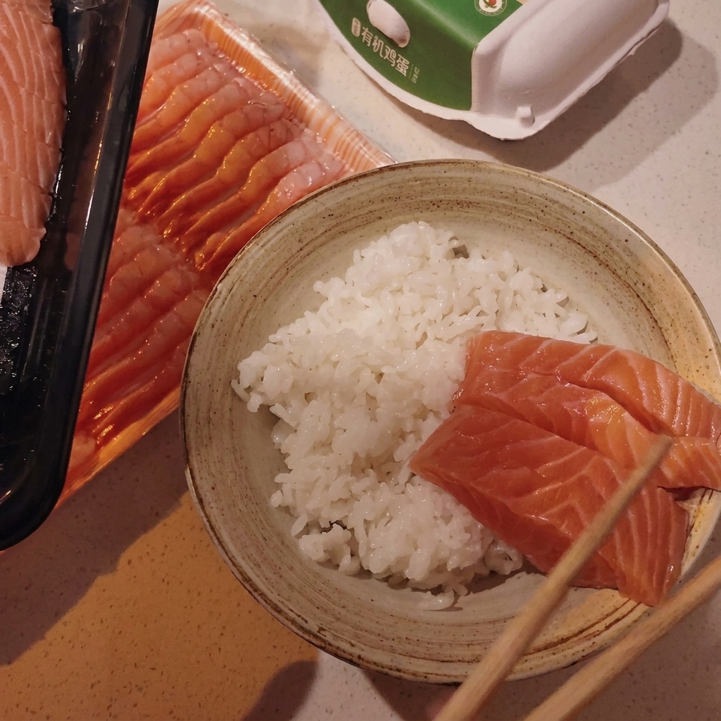 Roher Lachs und Jakobsmuscheln werden mit Stäbchen auf dem Reis in einer Schüssel angeordnet.