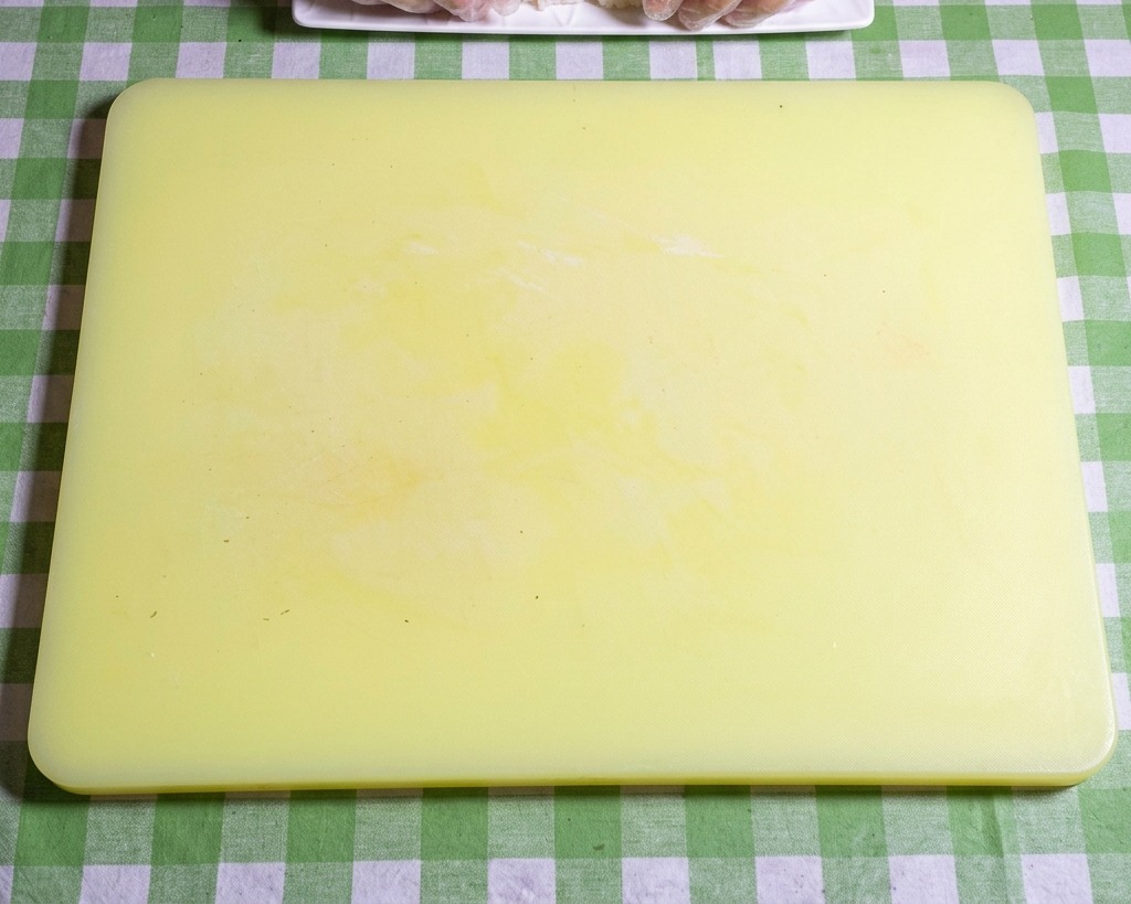 Nahaufnahme von behandschuhten Händen, die klebrigen Sushireis auf einem gelben Schneidebrett zu gleichmäßigen ovalen Bällchen formen.