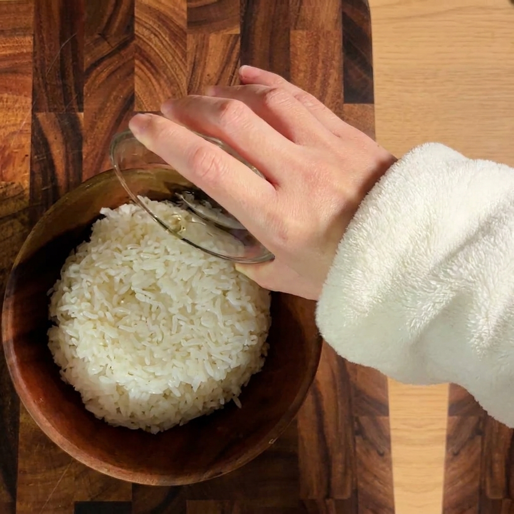 Gekochter weißer Reis wird in einer Holzschüssel mit Sushi-Essig gewürzt.