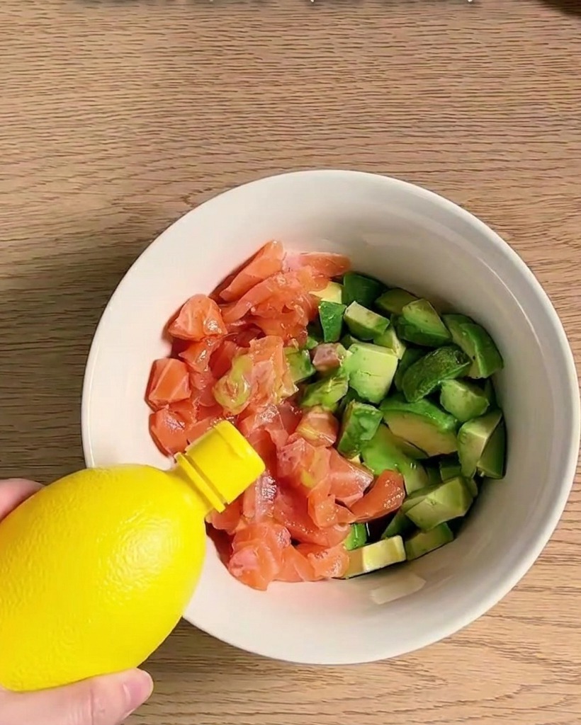 Eine Schüssel gefüllt mit Lachswürfeln und Avocadostücken, die gewürzt und mit verschiedenen Zutaten vermengt werden.