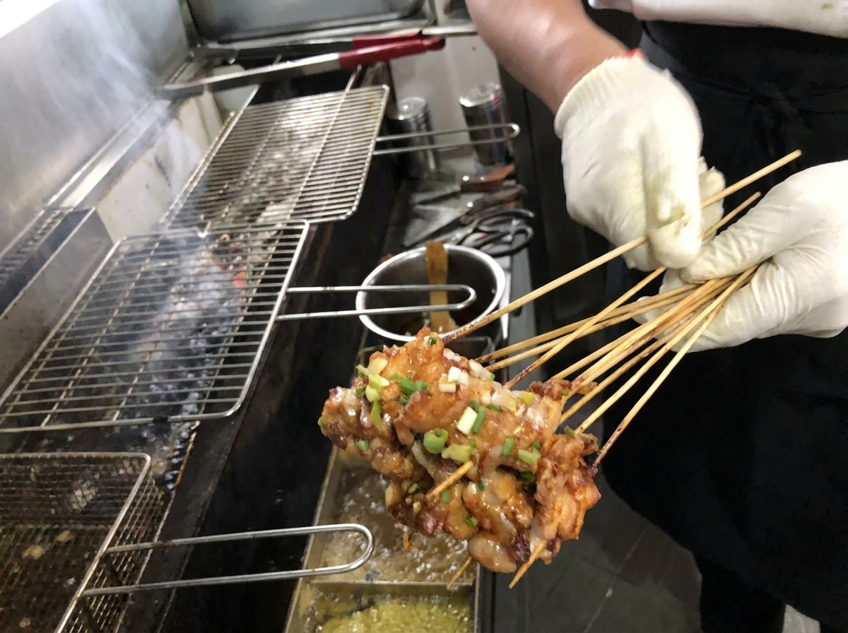 Nahaufnahme eines Pinsels, der eine reichhaltige braune Sauce auf golden gegrillte Schweinebauchspieße auf einem Holzkohlegrill aufträgt.