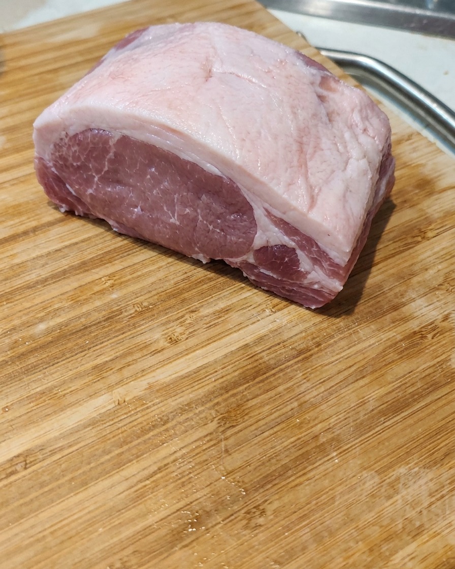 Nahaufnahme eines rohen Schweinebauchstücks, das auf einem Holzbrett in dicke, gleichmäßige Scheiben geschnitten wird.