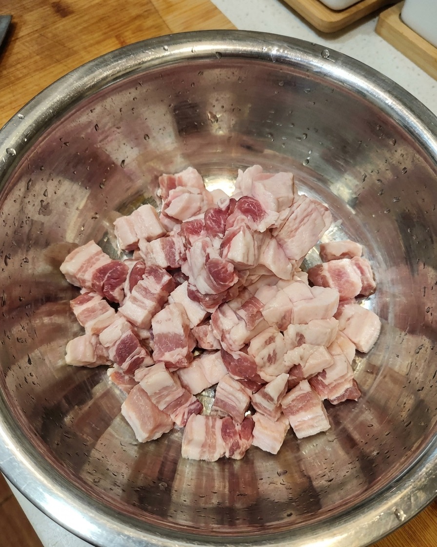 Rohe Schweinebauchscheiben liegen gemeinsam in einer großen Edelstahlschüssel.