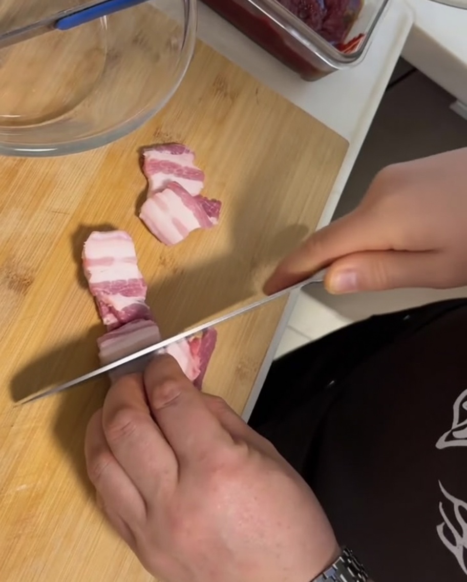 Dicke Scheiben von frischem, rohem Schweinebauch mit Schwarte auf einem Holzbrett neben einem Messer.