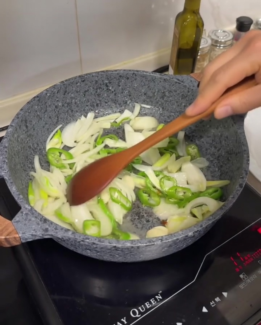 Geschnittene weiße Zwiebeln, grüne Chilis und Knoblauchzehen werden im ausgelassenen Fett angebraten.