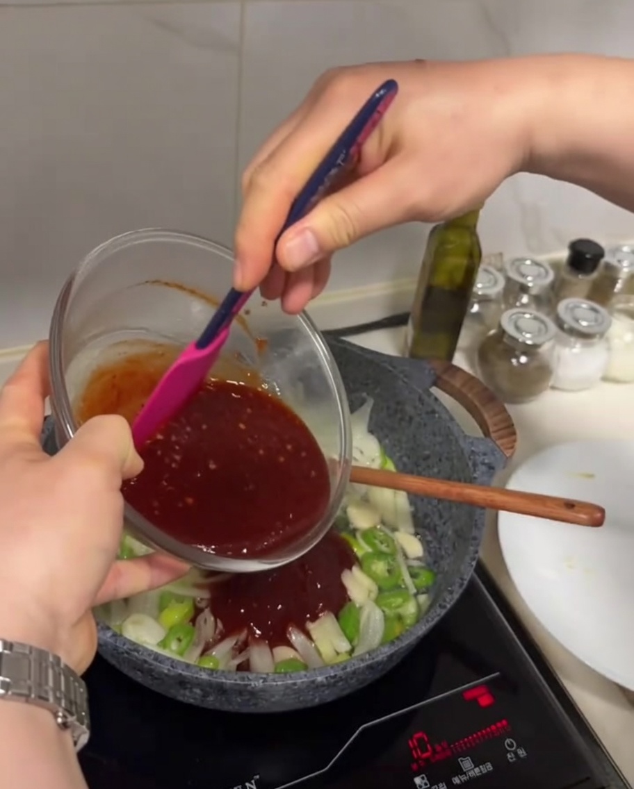 Die dunkelrote Soße wird aus einer Schüssel in die Pfanne zum angebratenen Gemüse gegossen.
