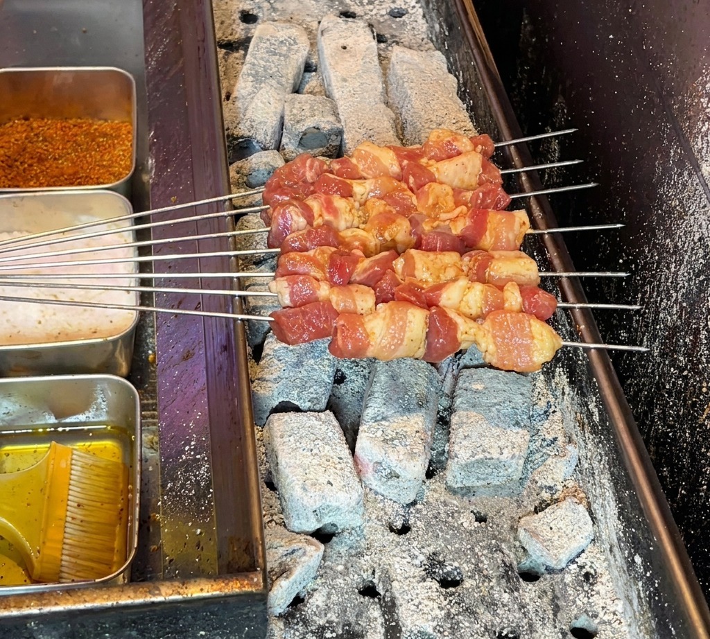 Aufgespießte rohe Schweinebauchwürfel auf einem heißen Holzkohlegrill, bereit zum Garen.