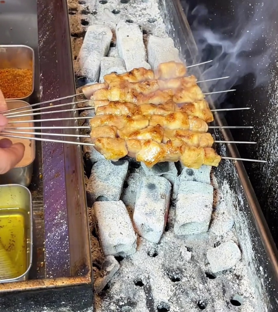 Schweinebauchspieße werden goldbraun und brutzeln über einem heißen, rauchigen Holzkohlegrill.