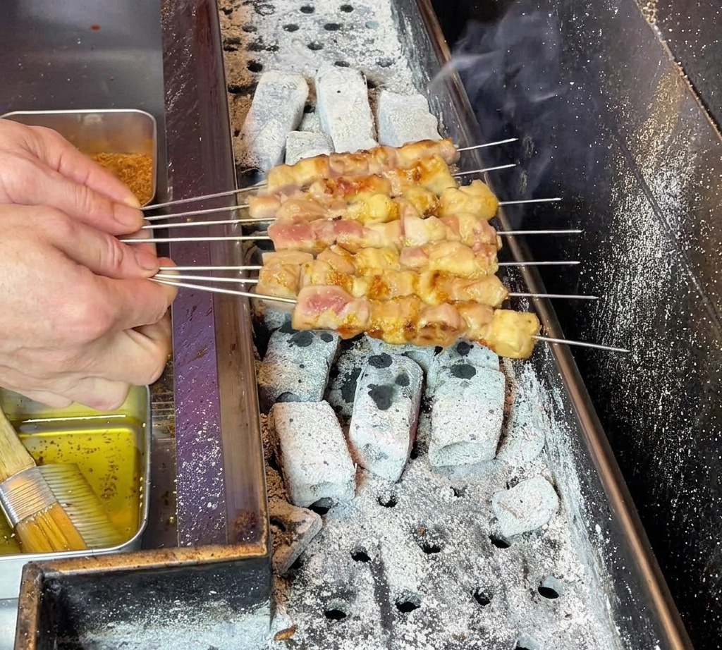 Die Hände des Kochenden bewegen die Spieße vorsichtig, um eine gleichmäßige Fettverteilung auf dem garenden Fleisch sicherzustellen.