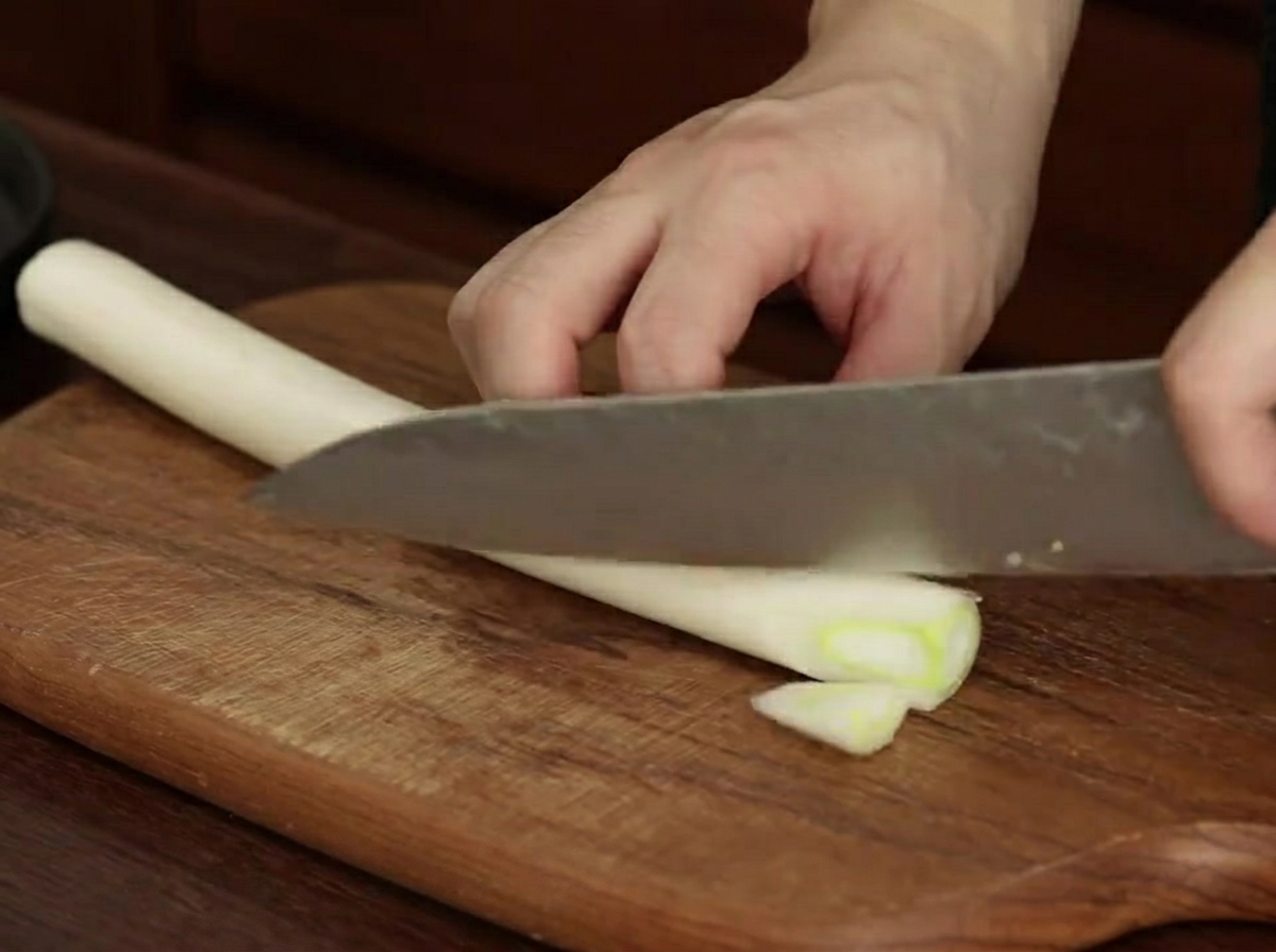 Neatly sliced diagonal pieces of green leek on the wooden cutting board.
