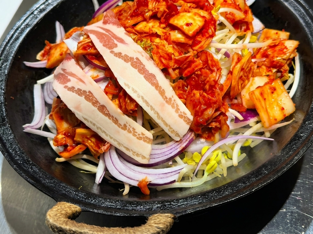 Scheiben von rohem Schweinebauch werden sorgfältig auf dem Bett aus Kimchi, Zwiebeln und Sojasprossen angeordnet.